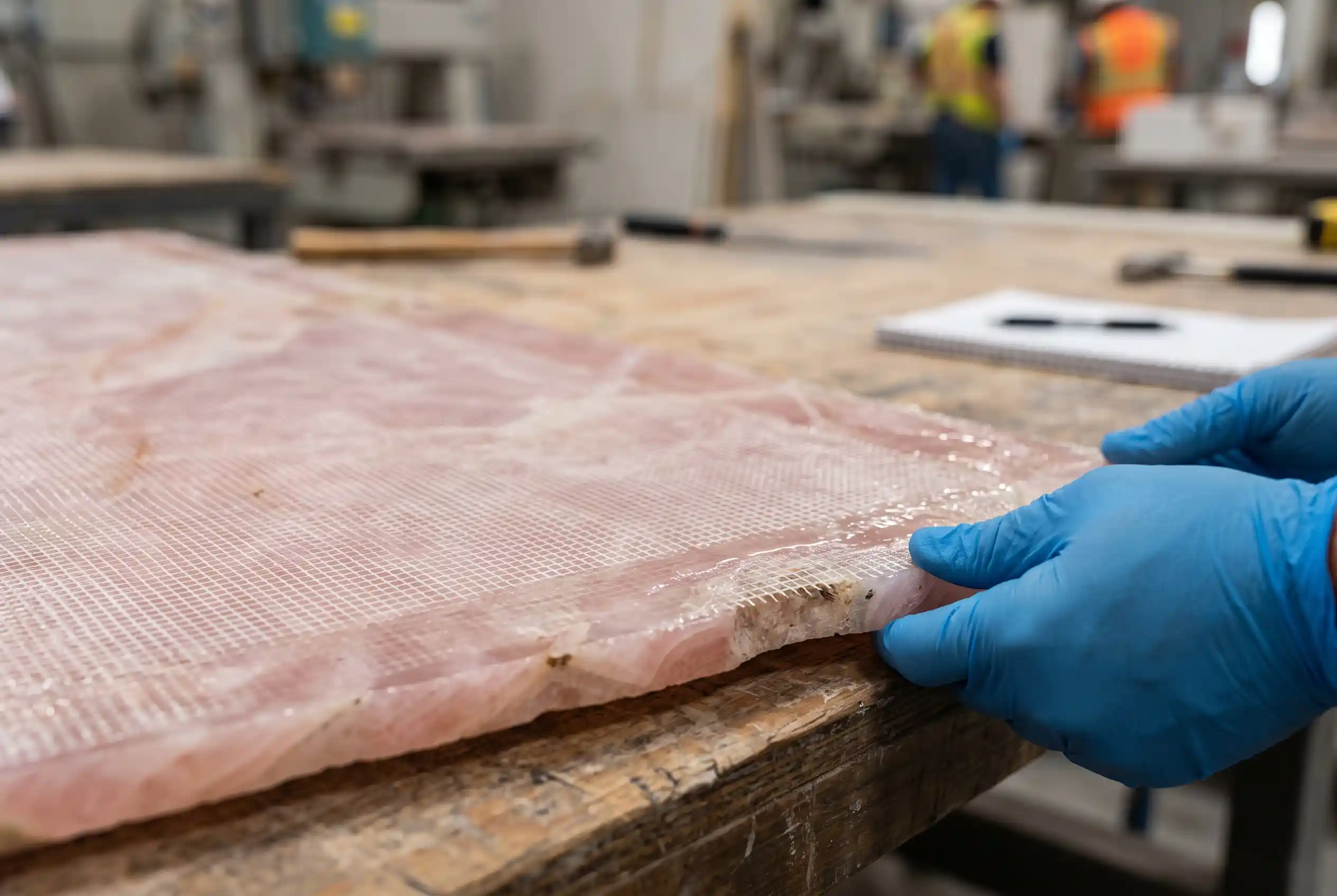 Close view of the back of a pink onyx slab during resin and mesh reinforcement inspection Close view of the back of a pink onyx slab during resin and mesh reinforcement inspection